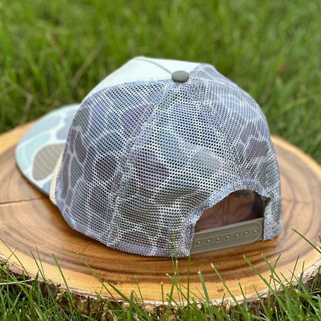 Back of trucker hat with 'Good Boy' logo on a wooden stump with grass in the background