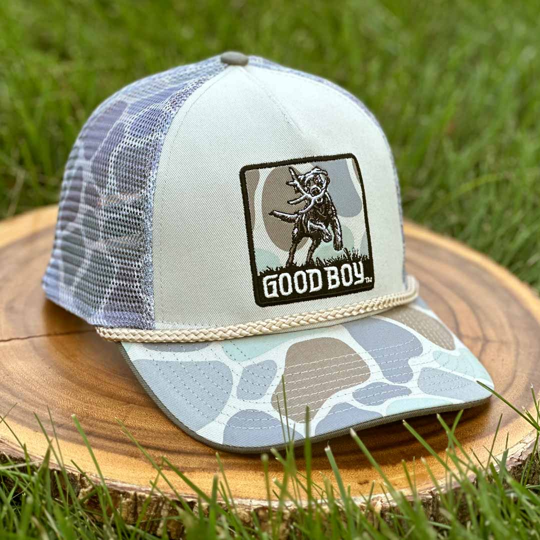 Trucker hat with 'Good Boy' logo on a wooden stump with grass in the background