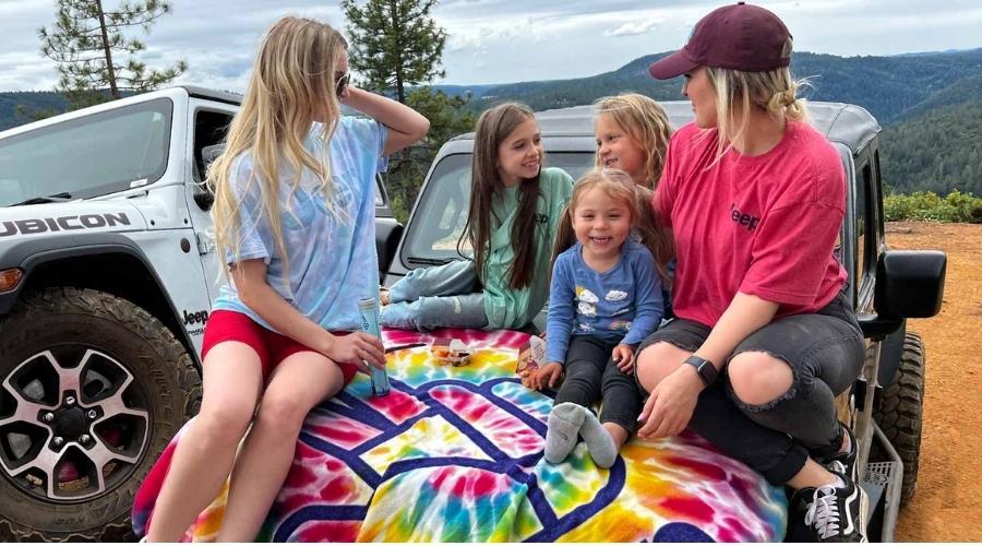family sitting on top of the hood of their jeep wrangler