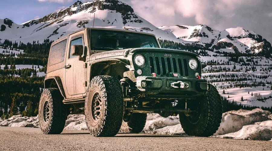 Green jeep driving down a snowy mountain