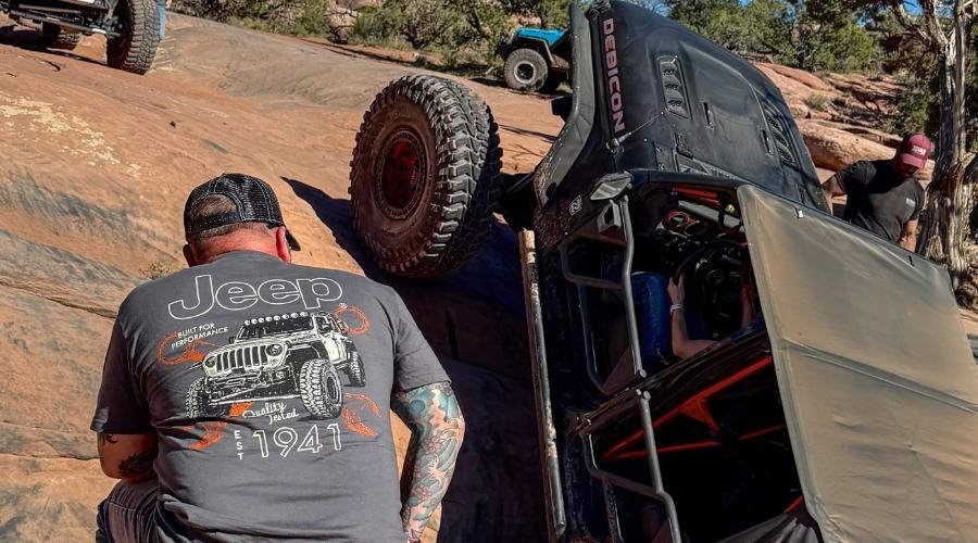 man looking at his jeep climbing some rocks
