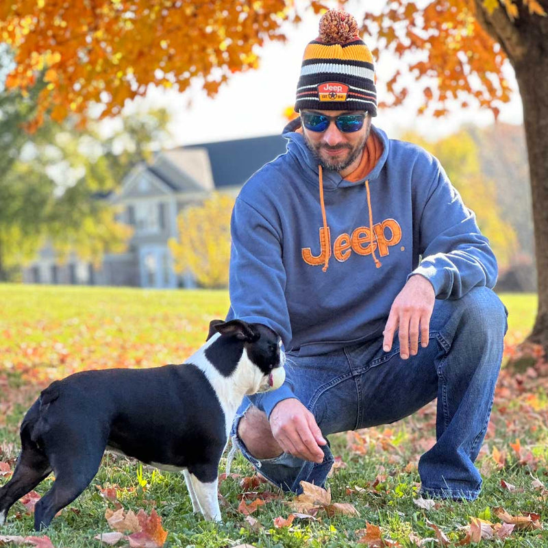 Man playing with dog and wearing Jeep vintage hoodie with embroidered orange jeep logo on front.