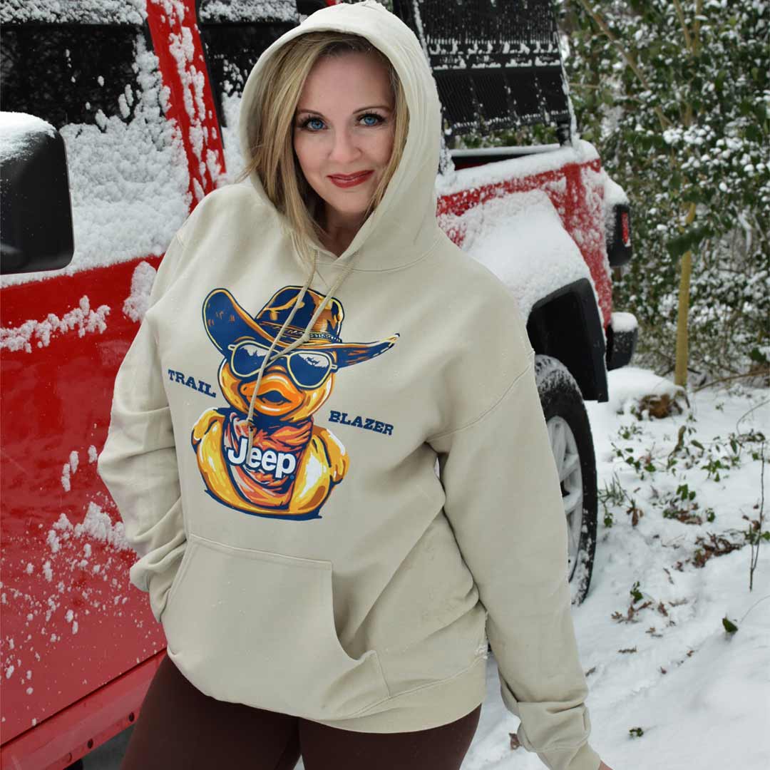 woman in front of a red jeep wearing a tan hoodie with a rubber duck, the Jeep logo, and "Trail Blazer" 