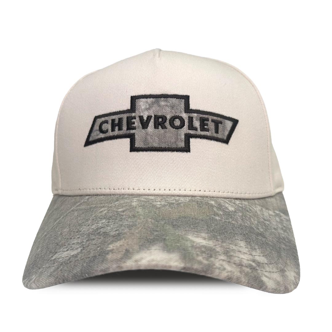 A baseball cap featuring an off-white front panel with a black and gray embroidered Chevrolet bowtie logo, and APX camouflage patterned brim.