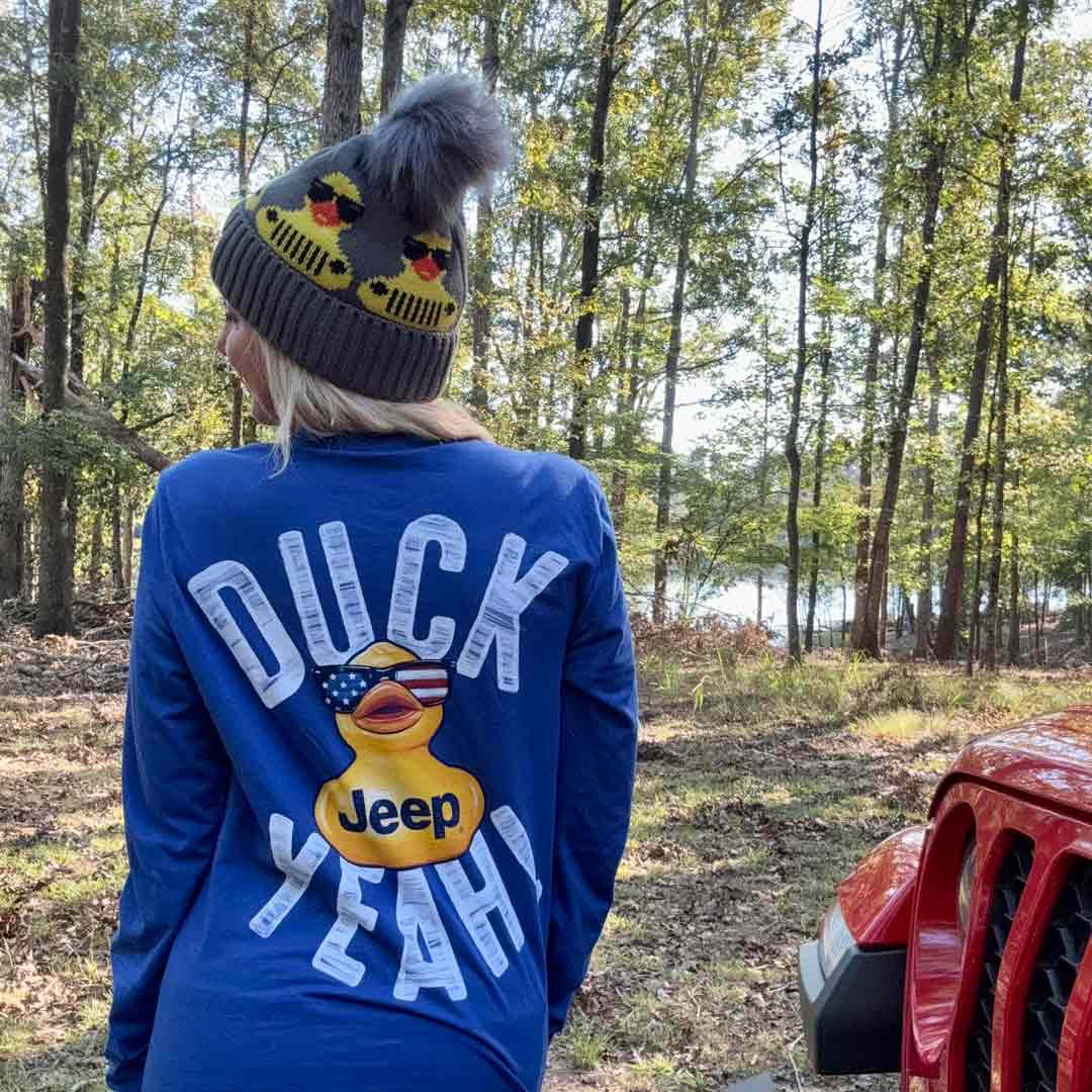 woman wearing a long sleeve shirt that has a large duck wearing American themed sunglsses on the back and says "duck yeah" with a duck jeep knit beanie hat